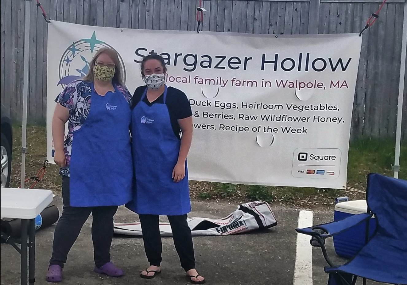 Meghan and her sister Hannah are at a farmers market, in front of the sign. They are wearing masks.